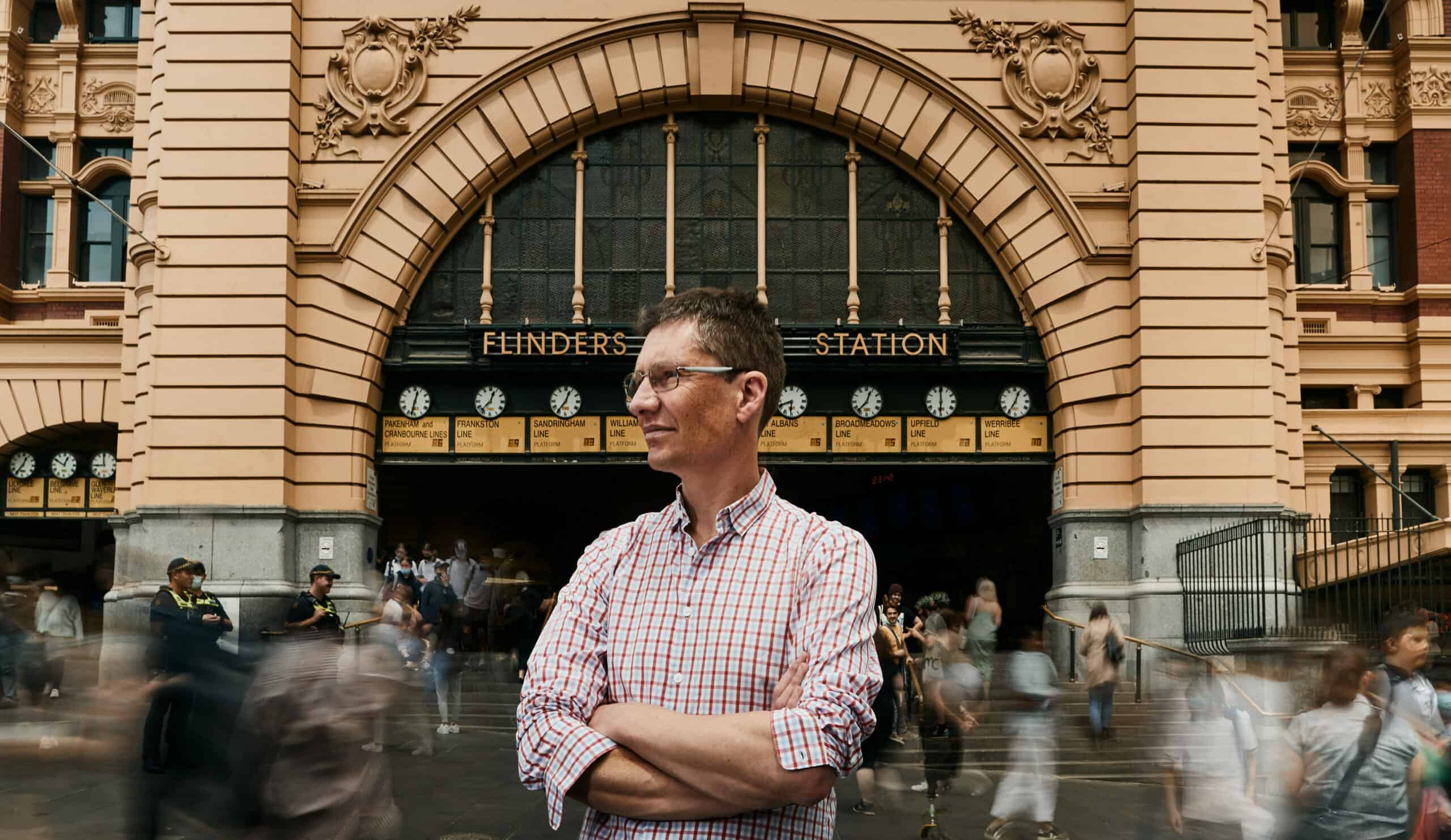 Professor James McCaw standing in front of the Edwardian Flinders Street railway station in Melbourne with people streaming past him