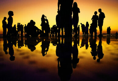 A thin layer of water reflecting the silhouettes of a group of people standing on it at dusk