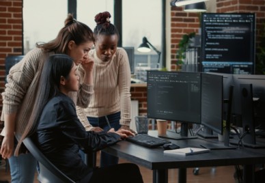 Three people gathering around a computer with code on the monitor, one of them typing