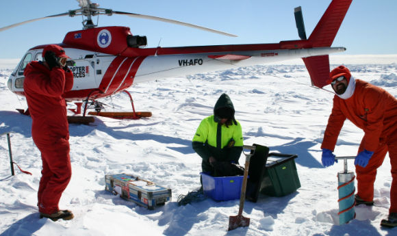ACEAS scientists working in Antarctica on the ice with a red helicopter in the background