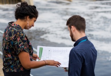 Two people talking next to a dam looking at plans