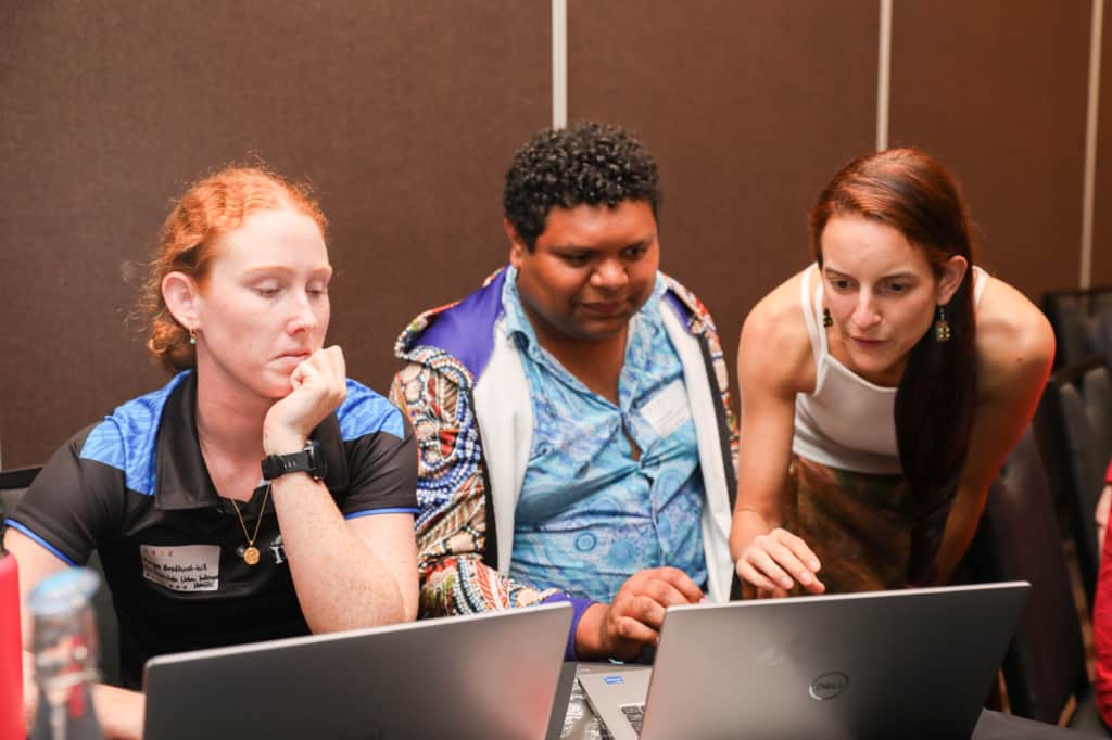 Three attendees looking at 2 laptops