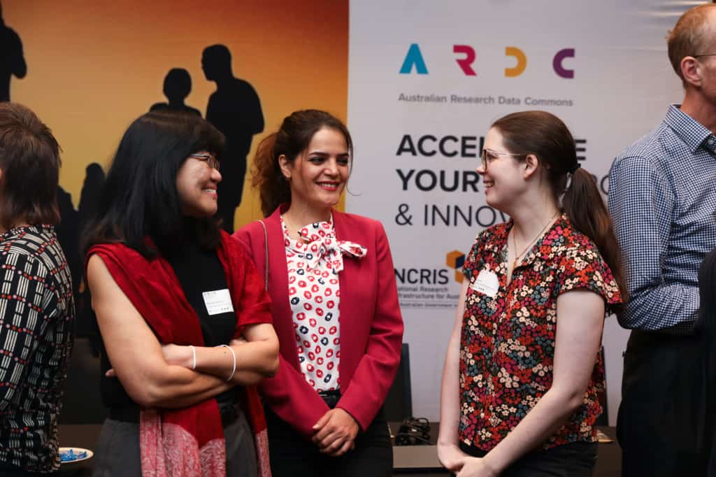 Three attendees having a conversation in front of the A R D C brand backdrop