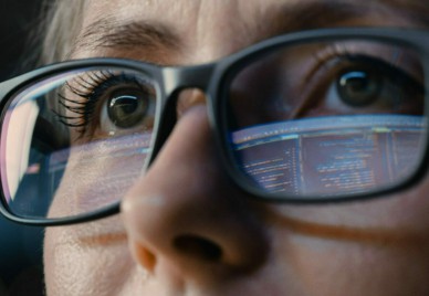 Close-up on an engineer with glasses refleting a computer screen full of code