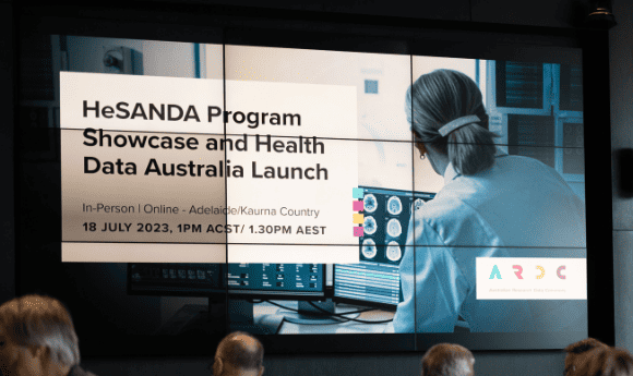 HeSANDA Program Showcase and Health Data Australia Launch - clinician looking at brain scan images in the background. Projected on a screen at a venue with tops of heads in the foreground.