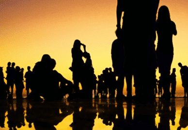 A thin layer of water reflecting the silhouettes of a group of people standing on it at dusk