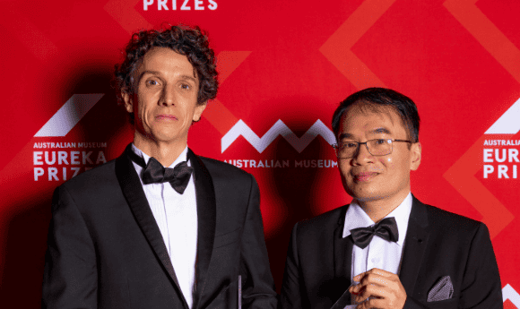 Dr Minh Bui and Professor Robert Lanfear from The Australian National University stand with their Eureka Prizes in black tie infront of a red background