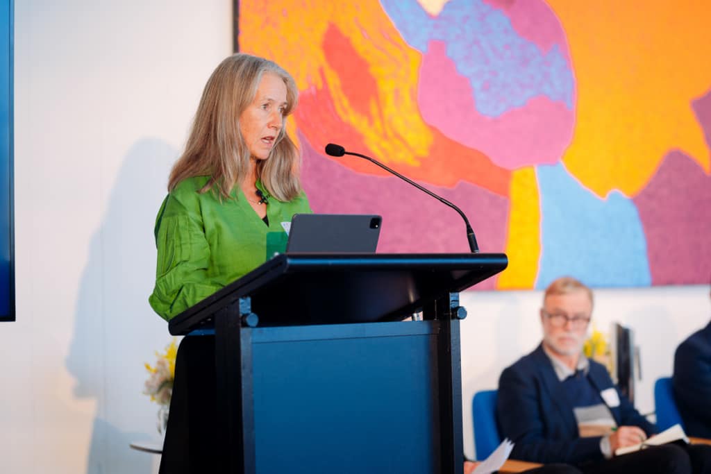Woman standing at a podium with a colourful painting in the background