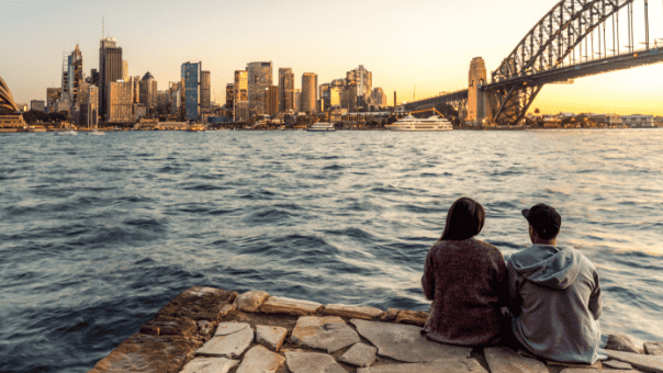 2 people sitting on rocks looking at Sydney harbour, including the Sydney Harbour Bridge and the city.