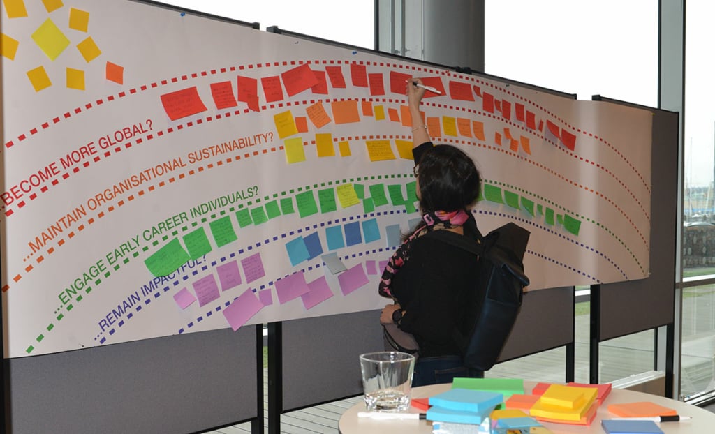 A person stands and looks at a display wall with a rainbow and post-it notes.