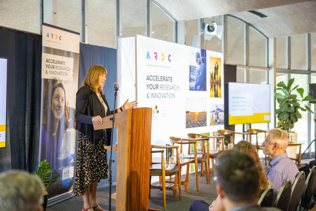 Rosie Hicks speaks in front of a crowd at the leadership forum, with ARDC banners behind.