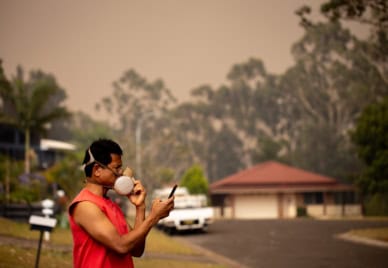 A person wearing a heavy-duty mask with a bushfire looming