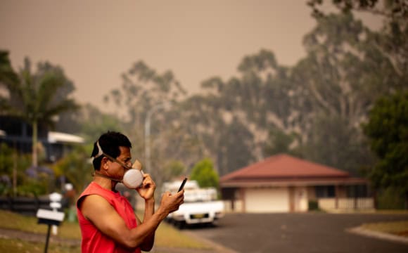 A person wearing a heavy-duty mask with a bushfire looming