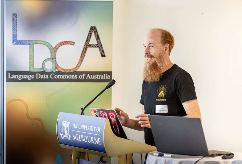 Ben Foley speaking at a University of Melbourne branded podium next to a pull-up banner for the L DaCA project